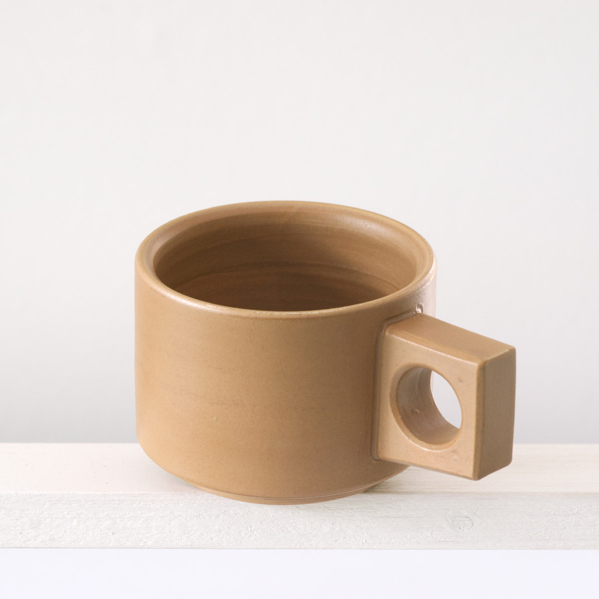 Schräge Ausicht auf eine kleine Tasse mit einer matten, karamellfarbenen Glasur